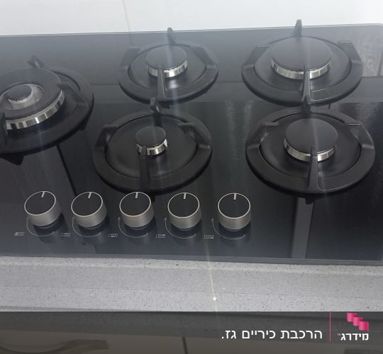 כיריים גז עם חמישה מבערים על משטח מטבח אפור